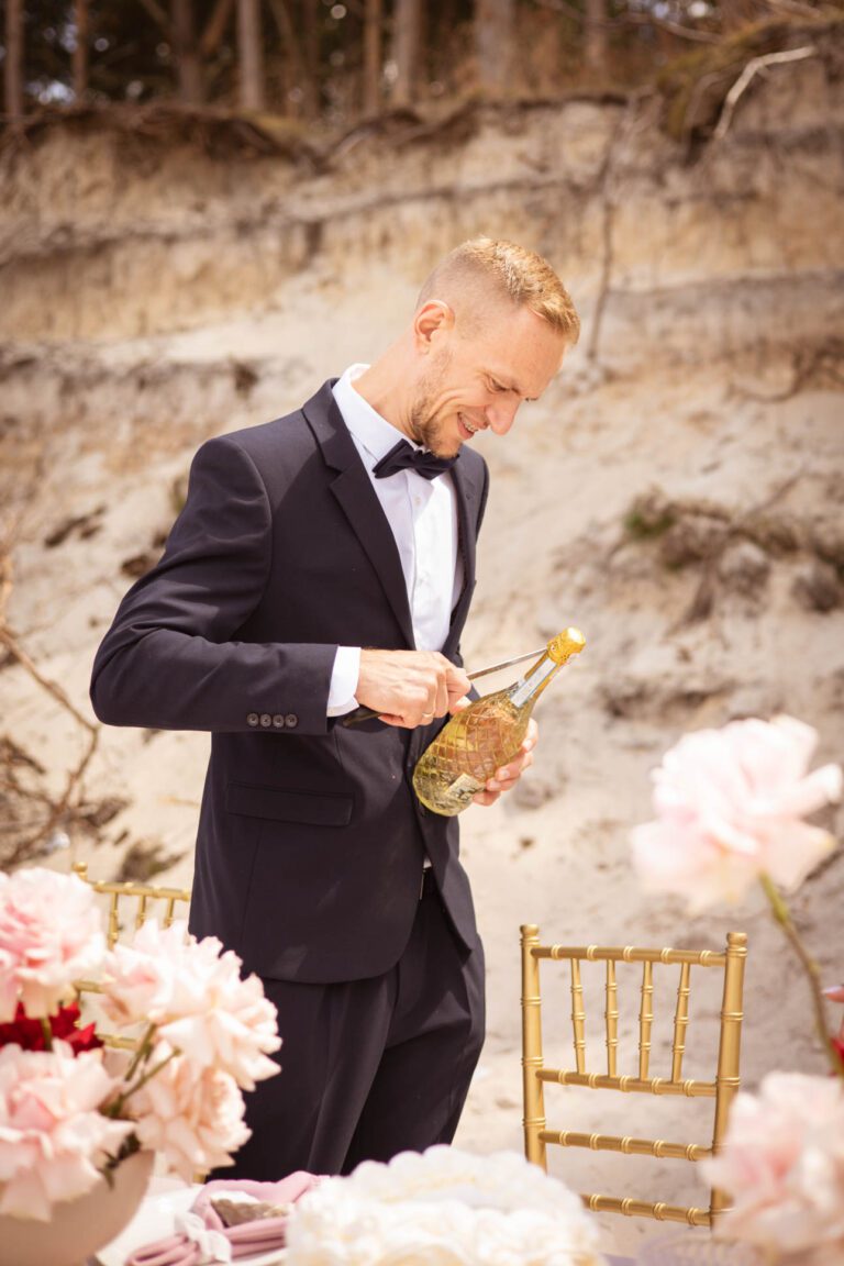 Pan młody otwiera szampana na plaży